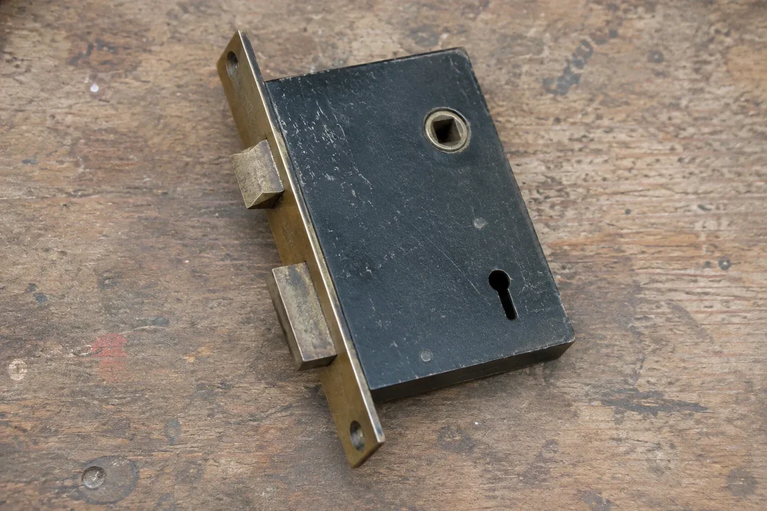 Closed mortise lock case with spindle opening, keyhole, latch and deadbolt on a wooden workbench. — Vintage Mortise Lock Service, Lawrence Park